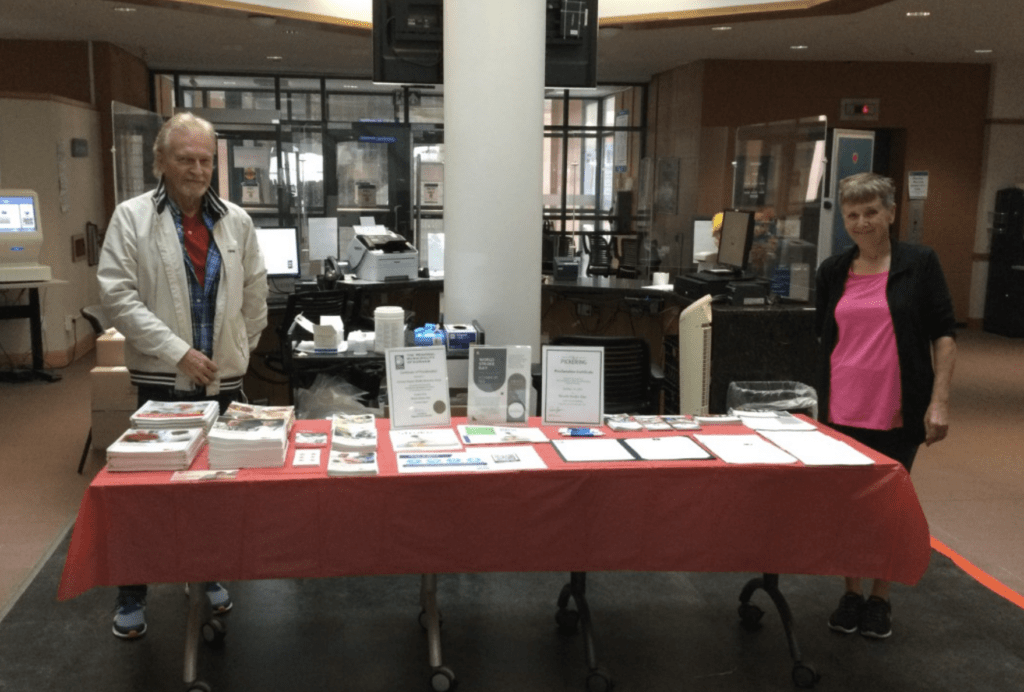 A woman and a man stand behind an information table