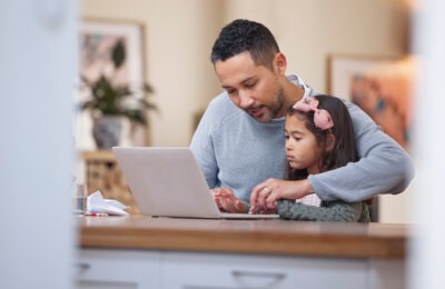 A father helps his daughter type on a laptop